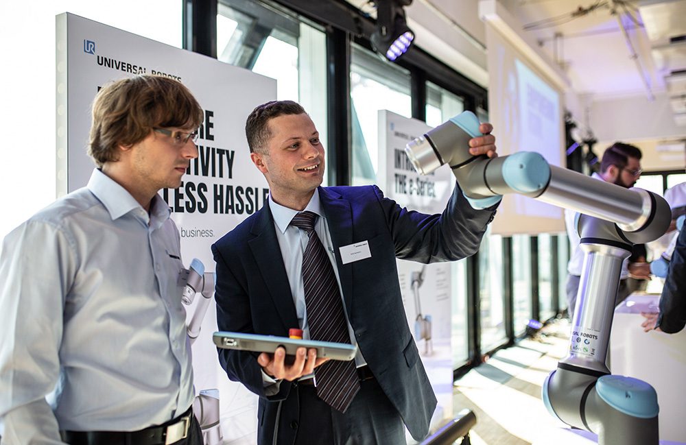 Two men examining a cobot from Universal Robots at a trade show.