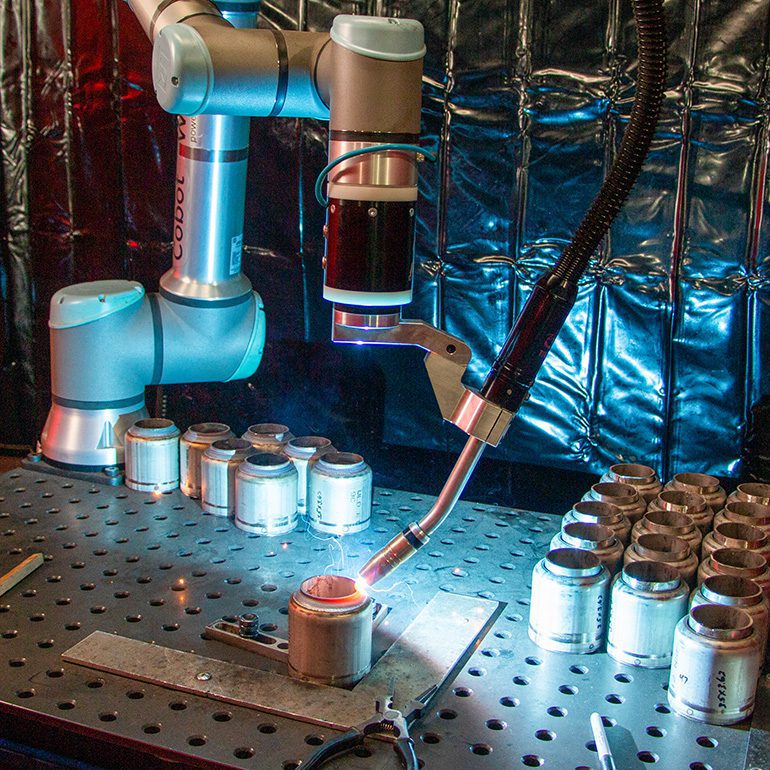 close up of a UR cobot equipped with a welder, mid path during a welding operation.